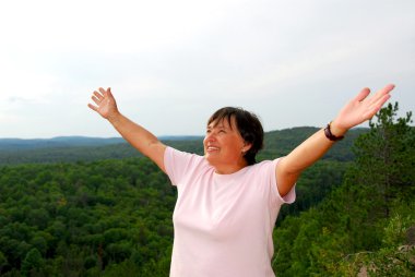 Mature woman on hilltop raising her arms clipart