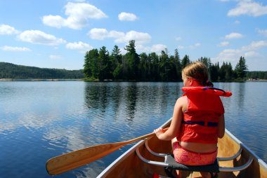 Young girl in canoe paddling on a scenic lake clipart