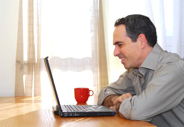 坐在他桌前用一台笔记本电脑 寻找快乐的人 — 图库照片