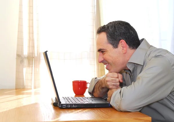 坐在他桌前用一台笔记本电脑 寻找快乐的人 — 图库照片
