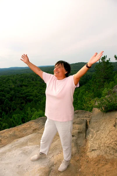 成熟的女人站在悬崖提高武器的喜悦 — 图库照片