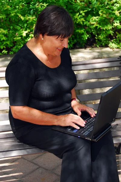 成熟的女人在室外的便携式计算机上键入 — 图库照片