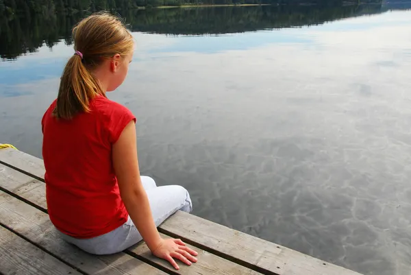 年轻的女孩浸洗的脚从边缘到湖里的一艘木船停靠 — 图库照片