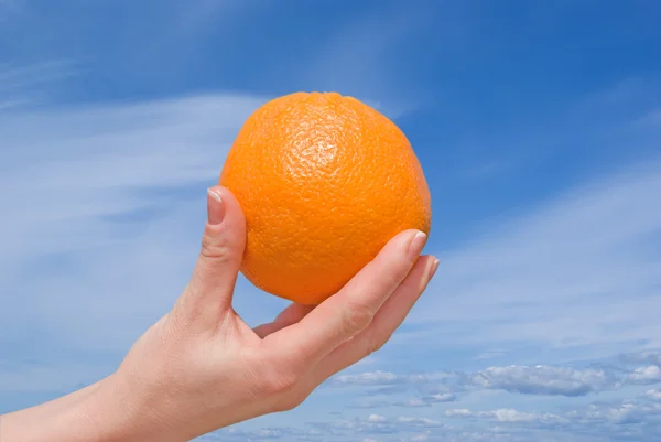 Mano con una naranja contra el cielo — Foto de Stock