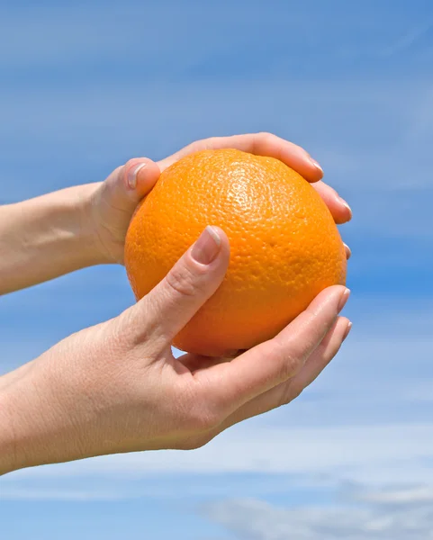 Händer med en orange mot himlen — Stockfoto