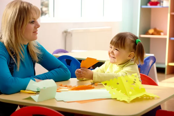 Учитель и маленькая девочка играют с цветной бумагой — стоковое фото