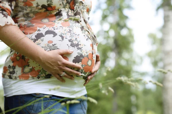 Женщина держит свой беременный живот на открытом воздухе — стоковое фото