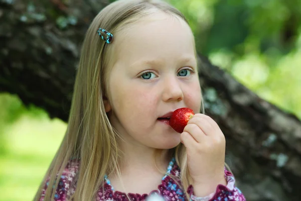 Happy little girl eating a strawberry. — Stock Photo, Image