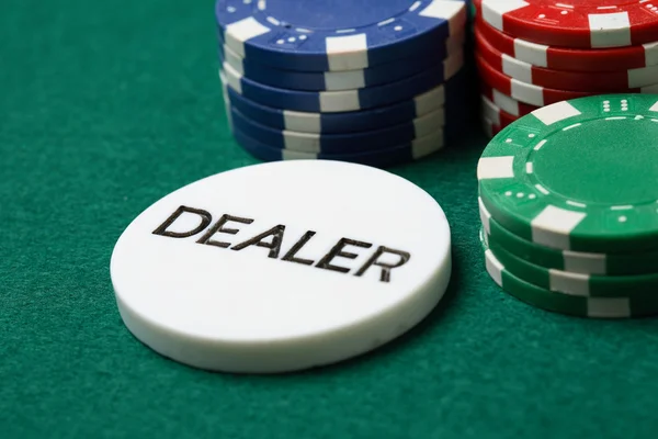 Bouton du distributeur et jetons de poker sur un vert — Photo