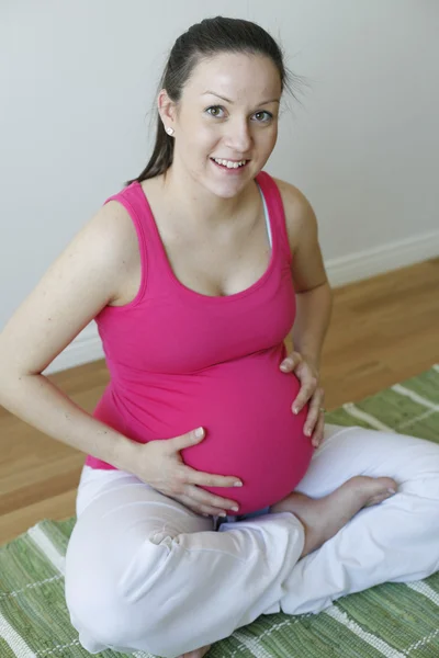 Jeune femme enceinte souriante tenant son — Photo