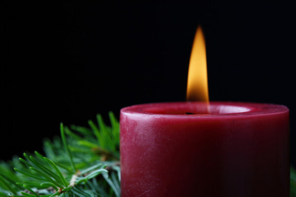 A close-up of a Christmas candle and a decorative fir branch in the dark creating a peaceful, tranquil and festive mood.