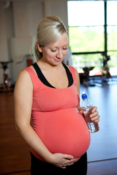 Těhotná žena uvolňující současně držet láhev s vodou. — Stock fotografie