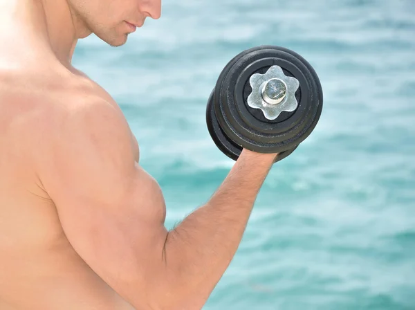 Мускулистый человек поднимает вес на пляже — стоковое фото