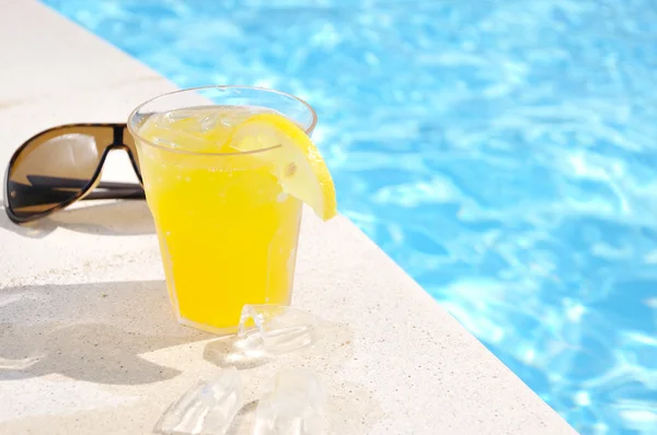 Sklenici šťávy a sluneční brýle u bazénu — Stock fotografie