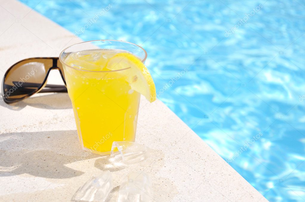 Glass of juice and sun glasses at the swimming pool