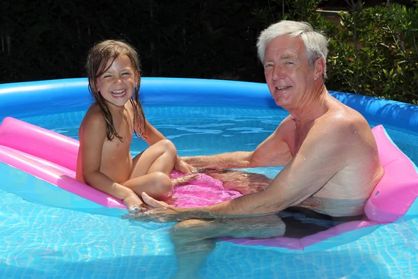 Granddaughter and grandfather floating on a lilo — Stock Photo, Image