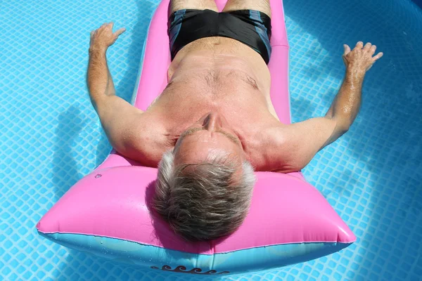 Hombre mayor tomando el sol en la piscina Imágenes de stock libres de derechos