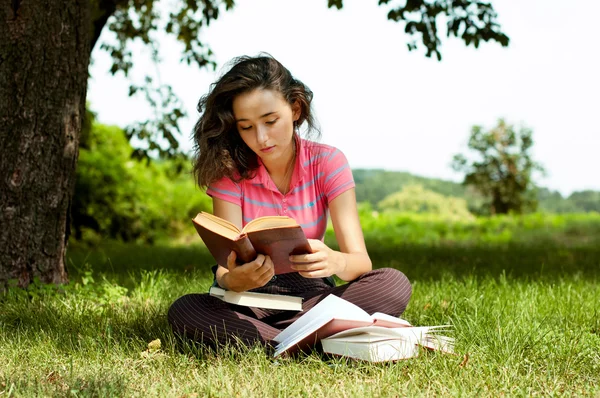 Het meisje met boeken zittend op een gras — Stockfoto