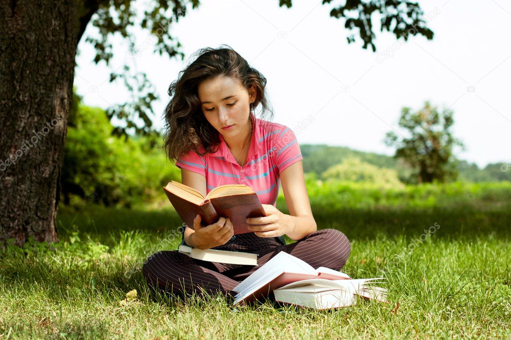 The girl with books sitting on a grass