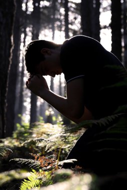 Man kneeling praying in the forest clipart