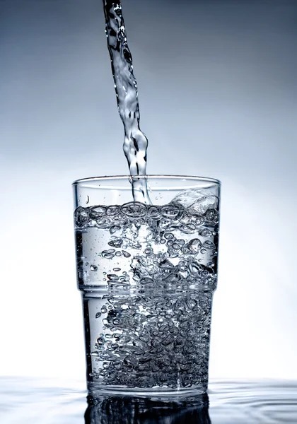 Nette glas staande op water met vloeistof — Stockfoto