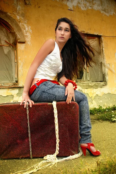 Krásný model sedí na červený kufr. — Stock fotografie