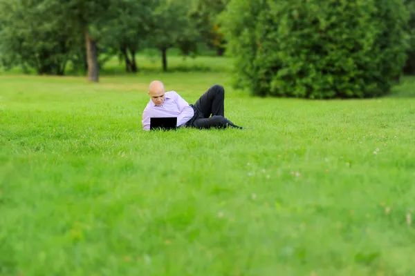Бізнесмен з ноутбуком лежить на зеленій траві — стокове фото