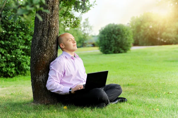 商人与坐在旁边一棵树的笔记本电脑 — 图库照片