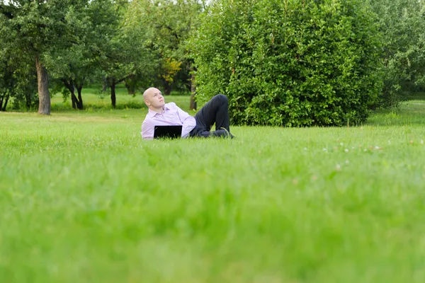 Mann mit Laptop liegt auf grünem Gras — Stockfoto