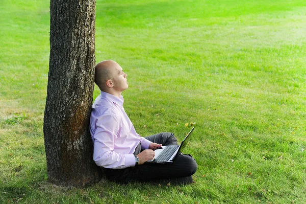 Uomo con computer portatile seduto vicino a un albero — Foto Stock