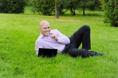 Man with laptop lying on green grass clipart