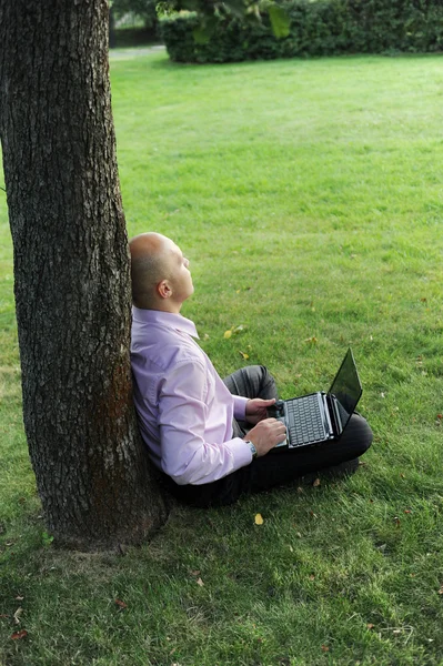 Hombre con portátil sentado cerca de un árbol —  Fotos de Stock