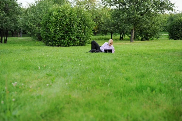 商人用躺在绿草地上的笔记本电脑 — 图库照片