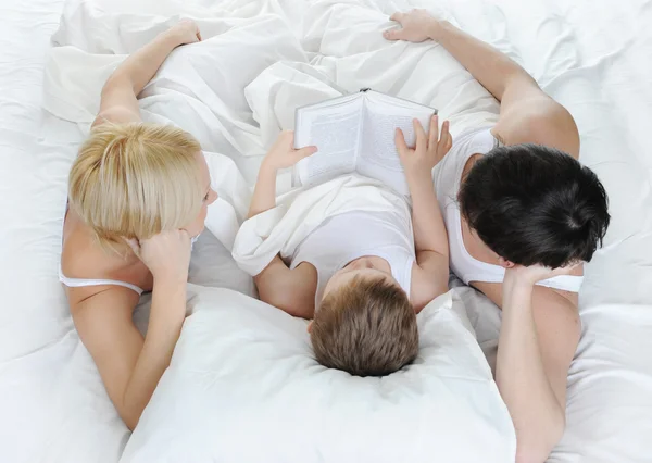 लड़का बिस्तर पर माता-पिता को एक किताब पढ़ता है रॉयल्टी फ़्री स्टॉक फ़ोटो