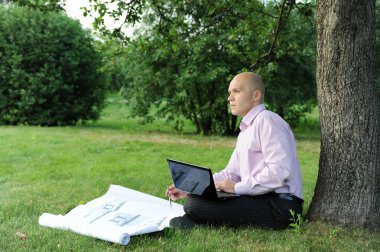 laptop bir ağaç Park yakınında oturan adam