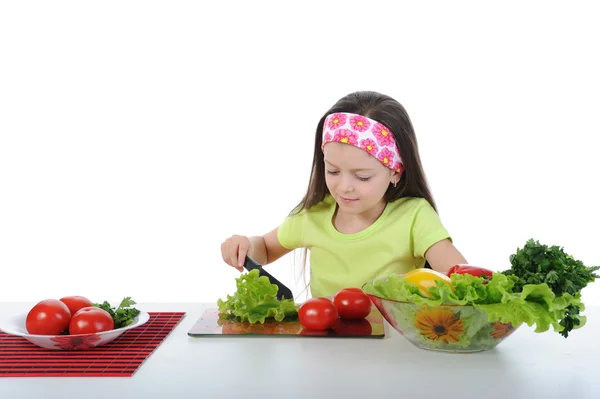 Liten flicka skär sallad vid bordet — Stockfoto