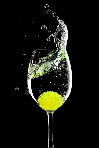 Schizzi in un bicchiere con palla di limone su uno sfondo nero — Foto Stock