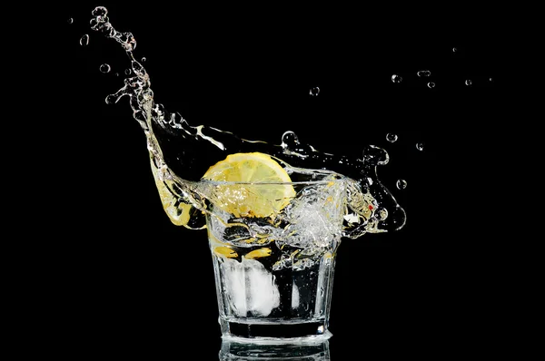 Всплеск в стакане с лимоном и льдом на черном фоне — стоковое фото