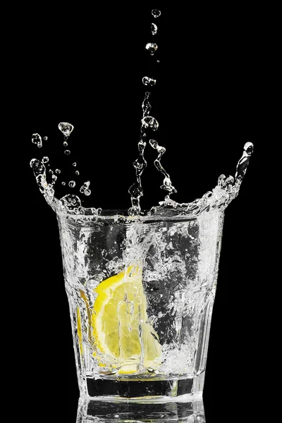 Splash in a glass with lemon and ice on a black background — Stock Photo, Image