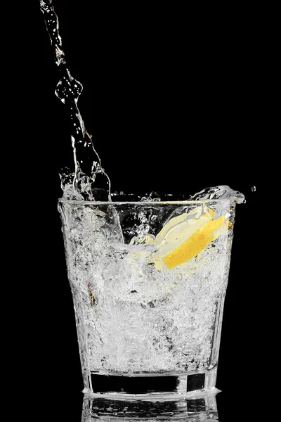 Versez dans un verre avec du citron et de la glace sur un fond noir — Photo
