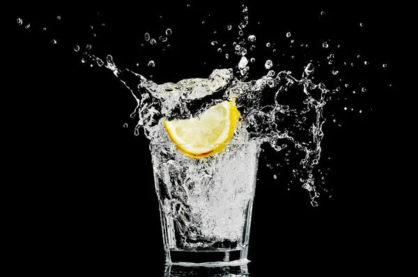 Всплеск в стакане с лимоном и льдом на черном фоне — стоковое фото