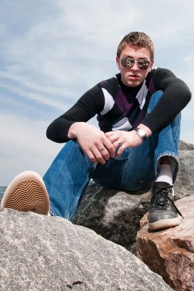 Young man on the rocks in clouds in the eyeglasses — Stock Photo, Image