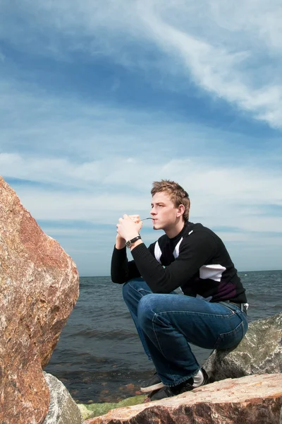 Jonge man op de rotsen op de achtergrond van de zee en de lucht — Stockfoto