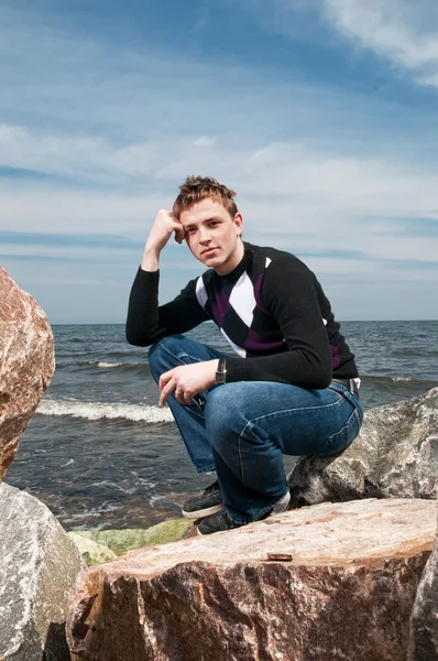 Młody człowiek na skałach na tle morza i nieba — Zdjęcie stockowe