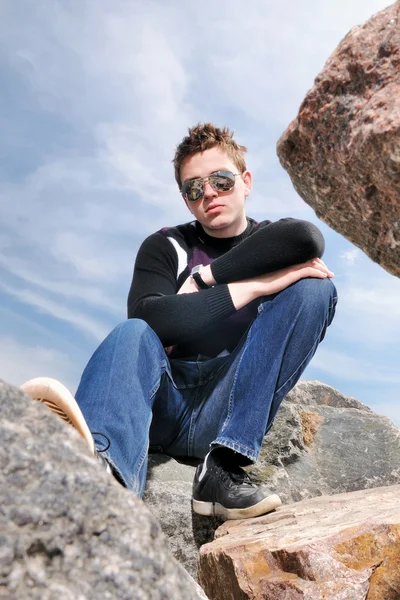 Молодой человек на скалах в облаках в очках — стоковое фото