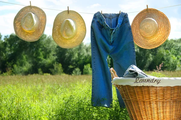 Blue jeans and straw hats on clothesline — Stock Photo, Image