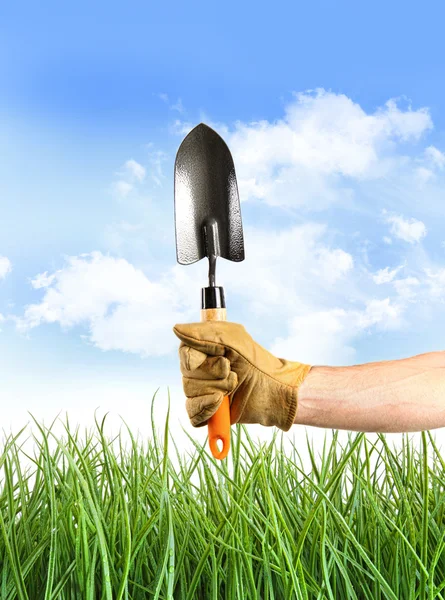 Рука держит садовую лопату на фоне голубого неба — стоковое фото