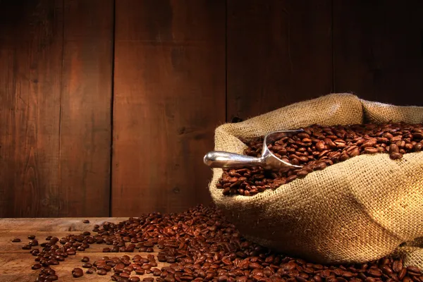 Saco de arpillera de granos de café contra madera oscura —  Fotos de Stock