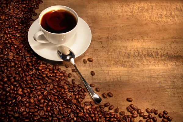 Vit kaffekopp med bönor på rustika bord — Stockfoto