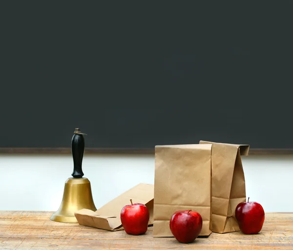 Sacos de almoço com maçãs e sino da escola na mesa — Fotografia de Stock